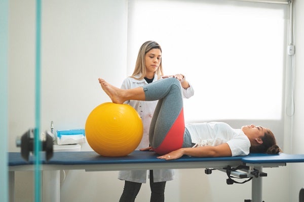 woman lying with her legs on exercise ball as the therapist guides her movement