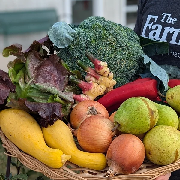 A wicker basket of different produce items, including broccoli, squash, onions and pears