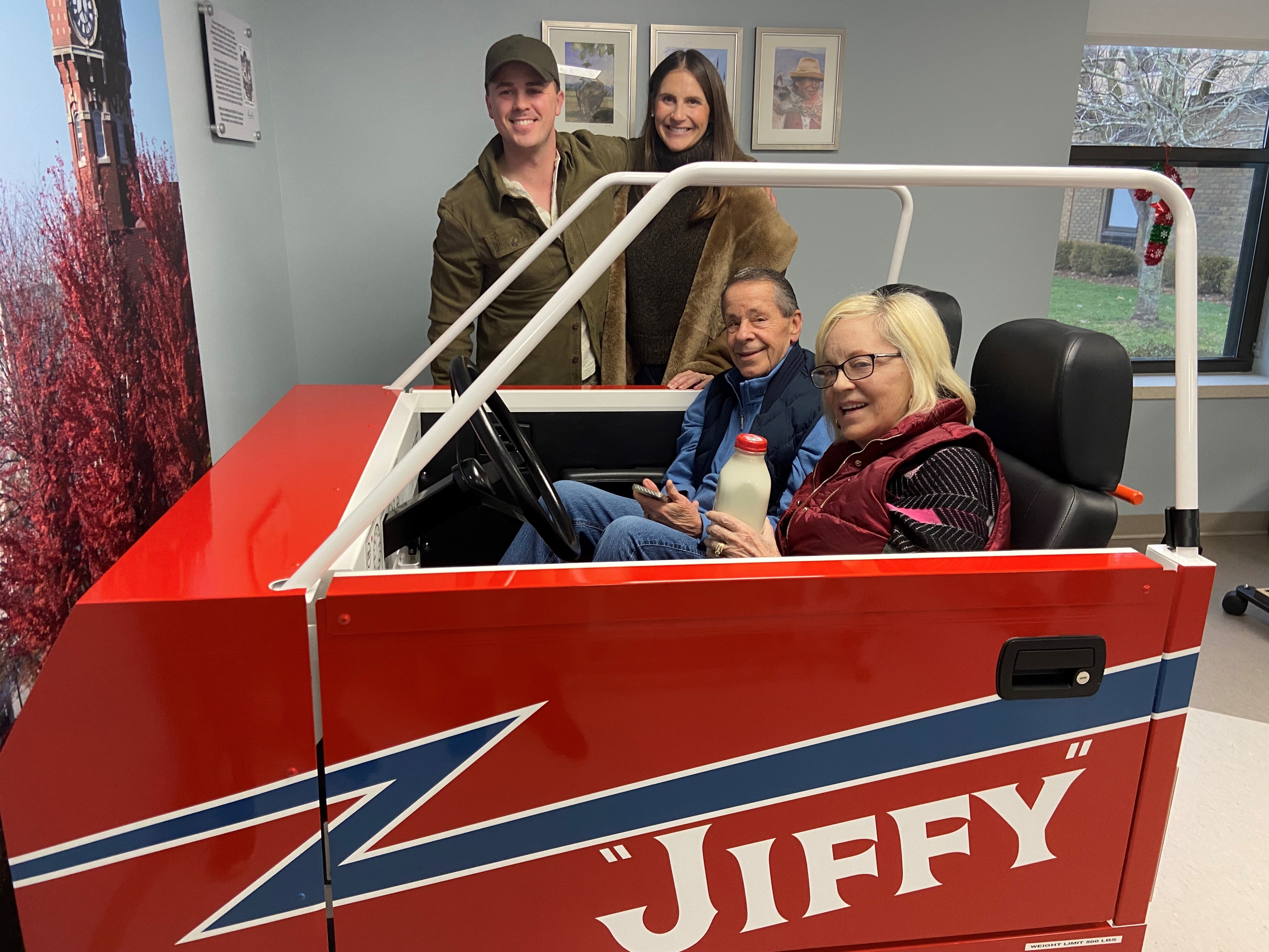 Two people sitting inside the car simulator and two people posing outside of it