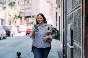 Woman reading on phone holding bag of produce