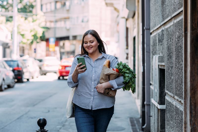 Woman reading on phone holding bag of produce