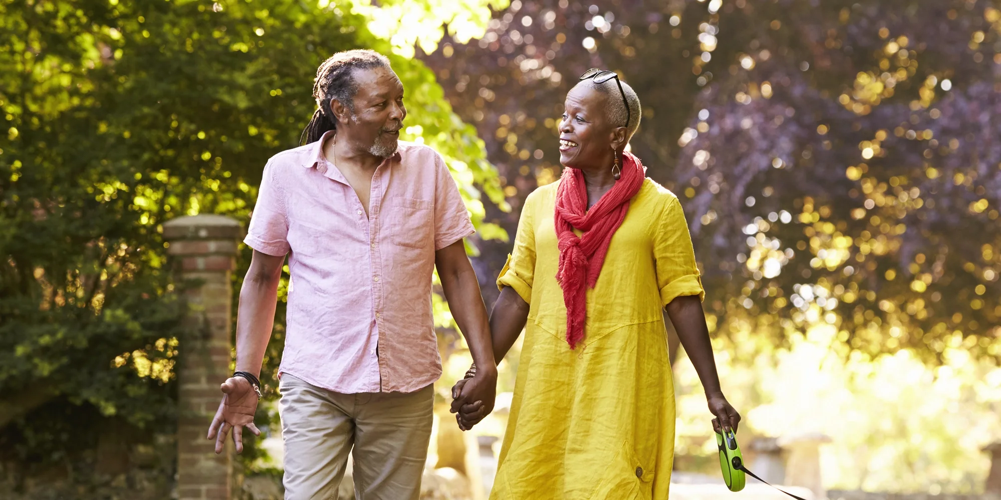 An aged couple holds hands while walking outside on a sunny day