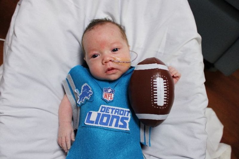 adorable infant dressed in Lions Jersey and football beside him