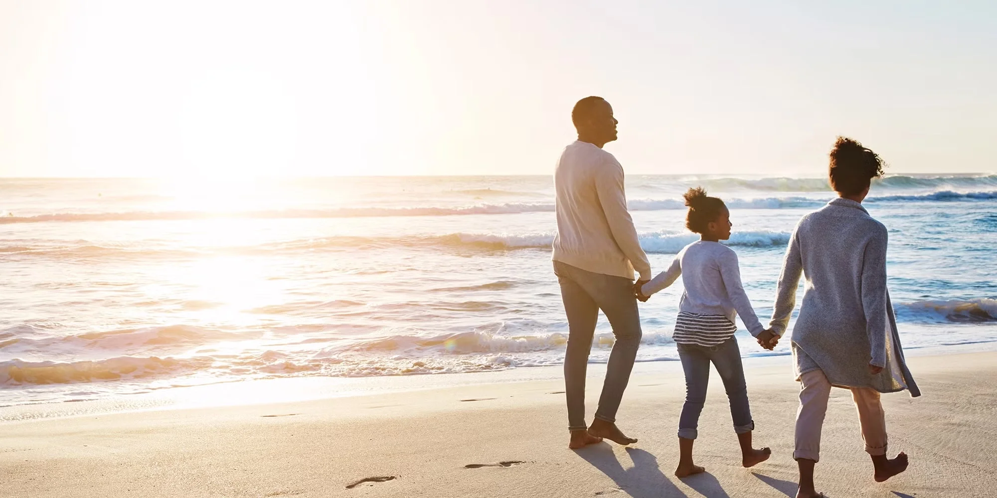 A family of three holds hand and walks down the shoreline