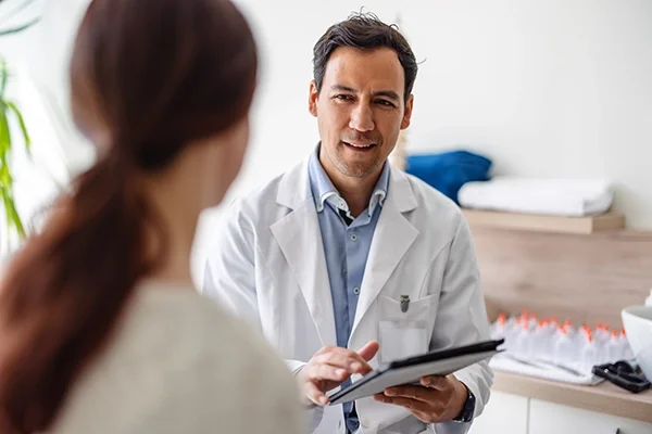 A doctor speaks to his patient, a woman wearing a ponytail
