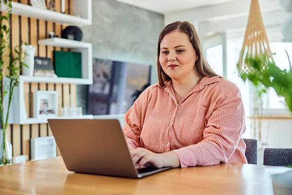 A woman in a pink sweatshirt sits at a laptop