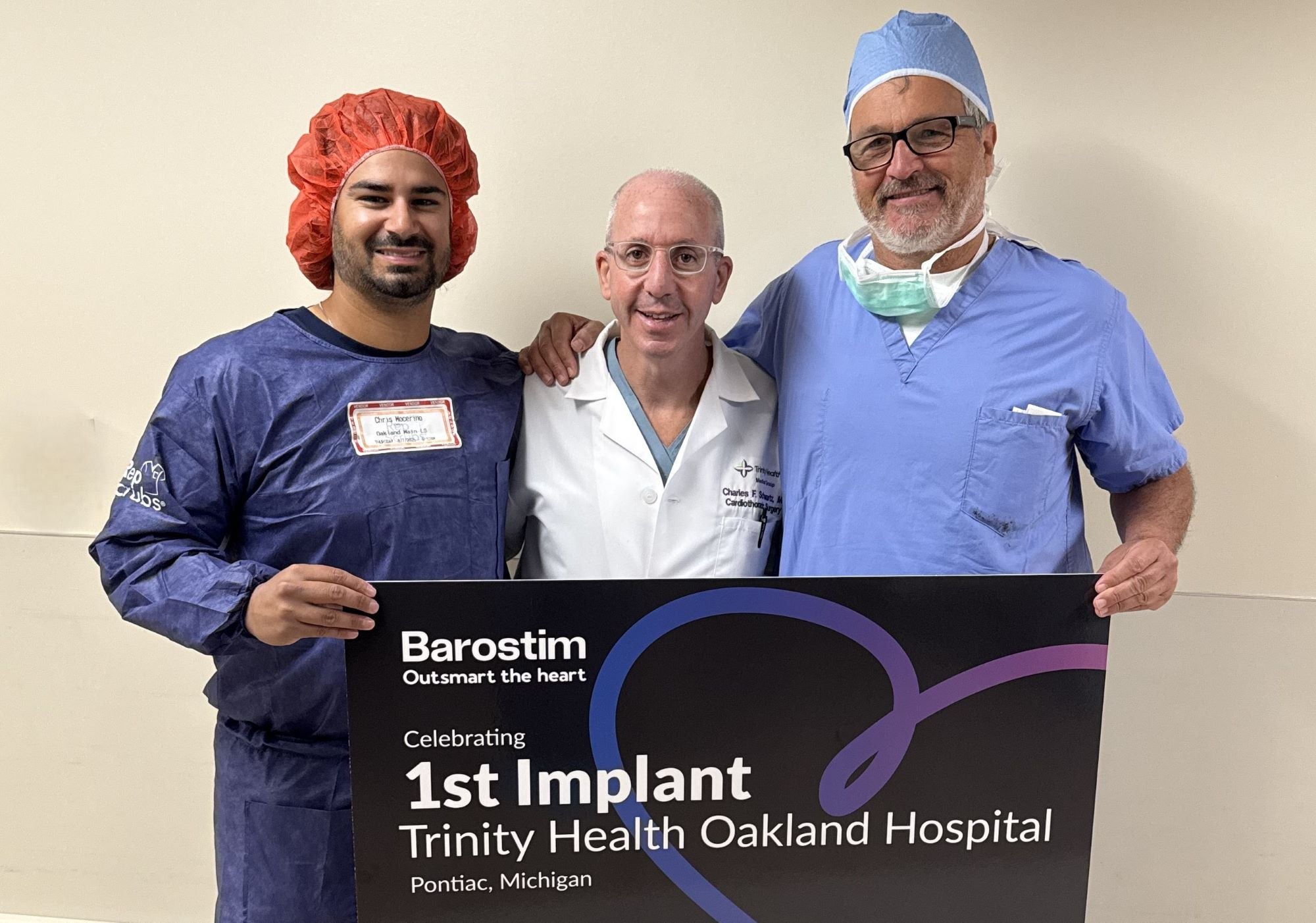 Three physicians in scrubs holding large sign that says '1st Implant'.