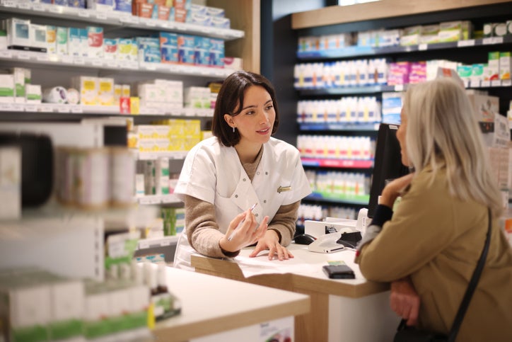 A female pharmacist discussing a prescription with an elderly lady customer at the service counter in a pharmacy.