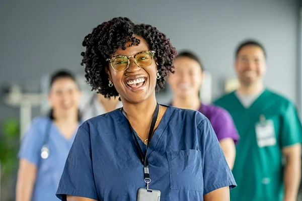 Four nurses in various scrub colors look toward the camera and smile