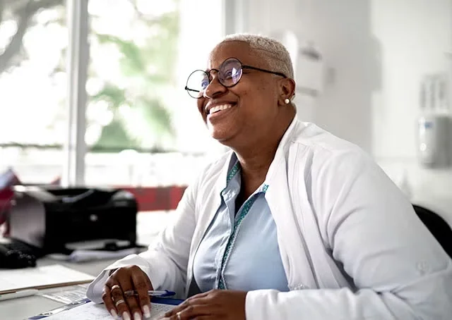 A doctor leans forward on her desk and smiles warmly