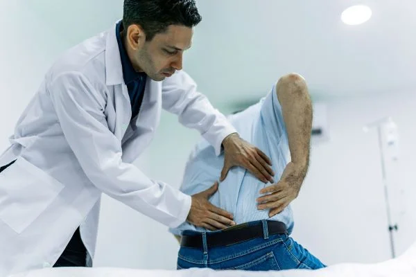 A doctor rests his hands upon an elderly man's back to treat his pain