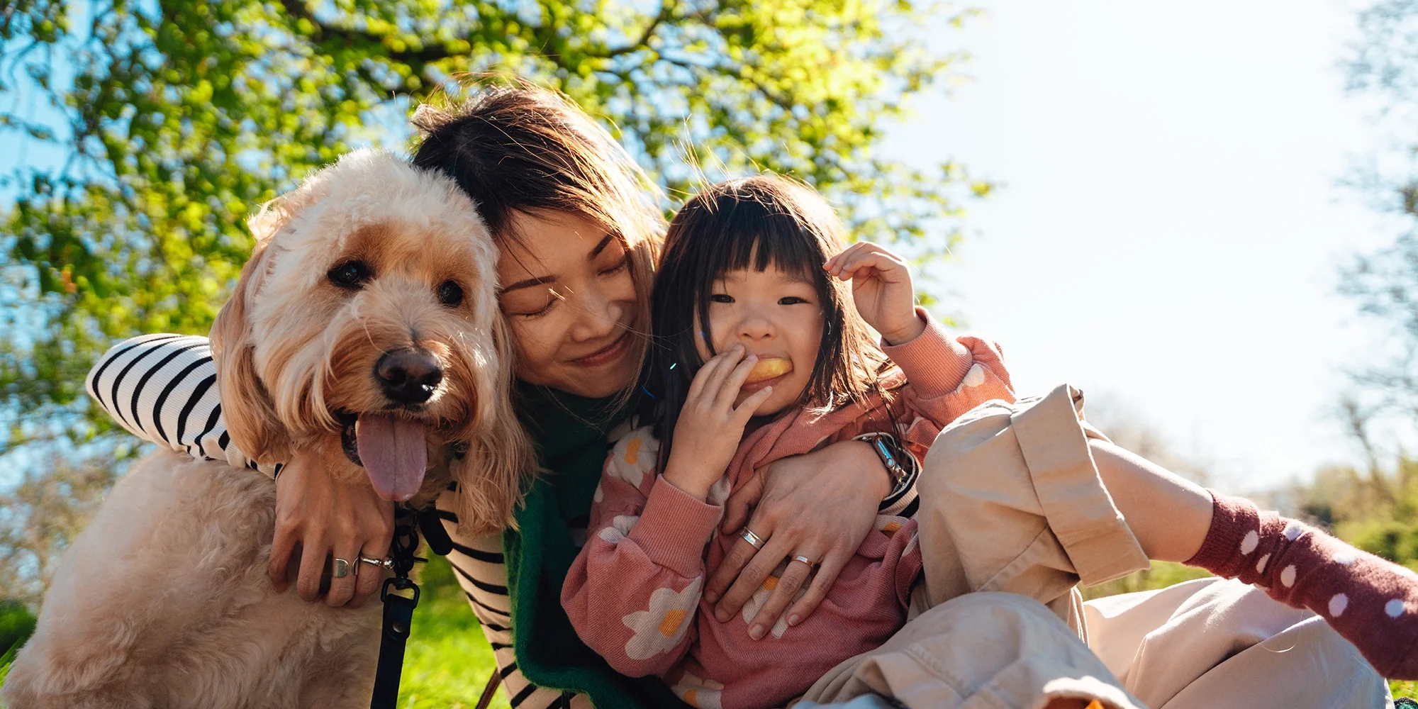 A mother and daughter hug outside with their dog