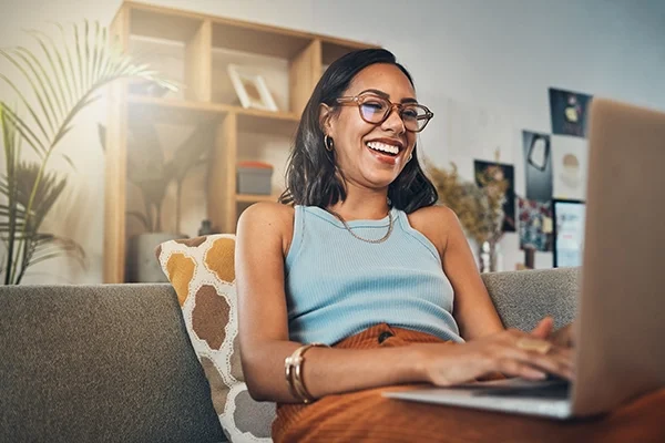 A woman smiles on her laptop as sunshine beams into her living room