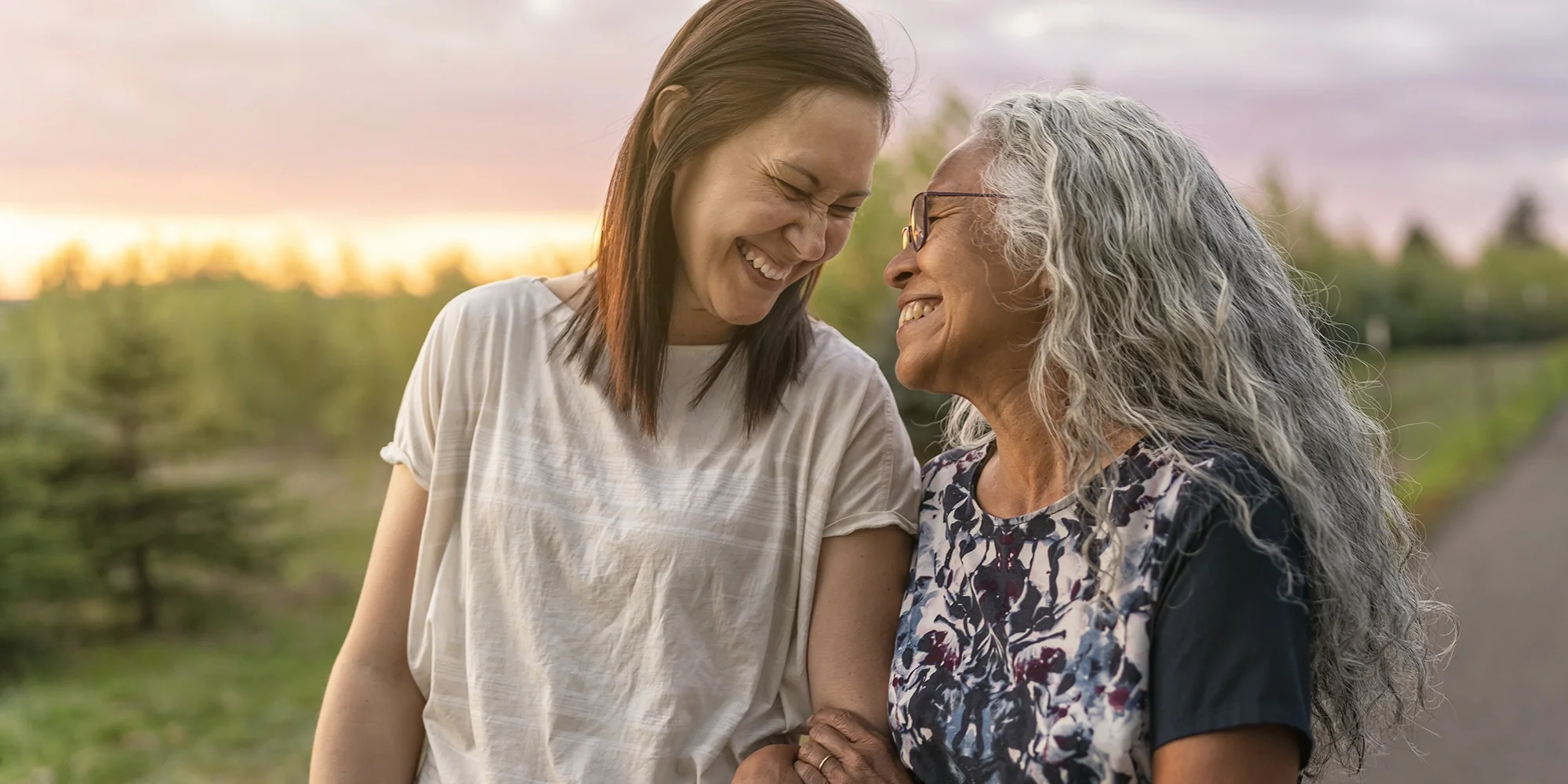 A senior woman takes an outdoor stroll at sunset with her daughter
