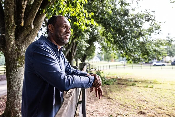 A man leans up against a fence overlooking a field