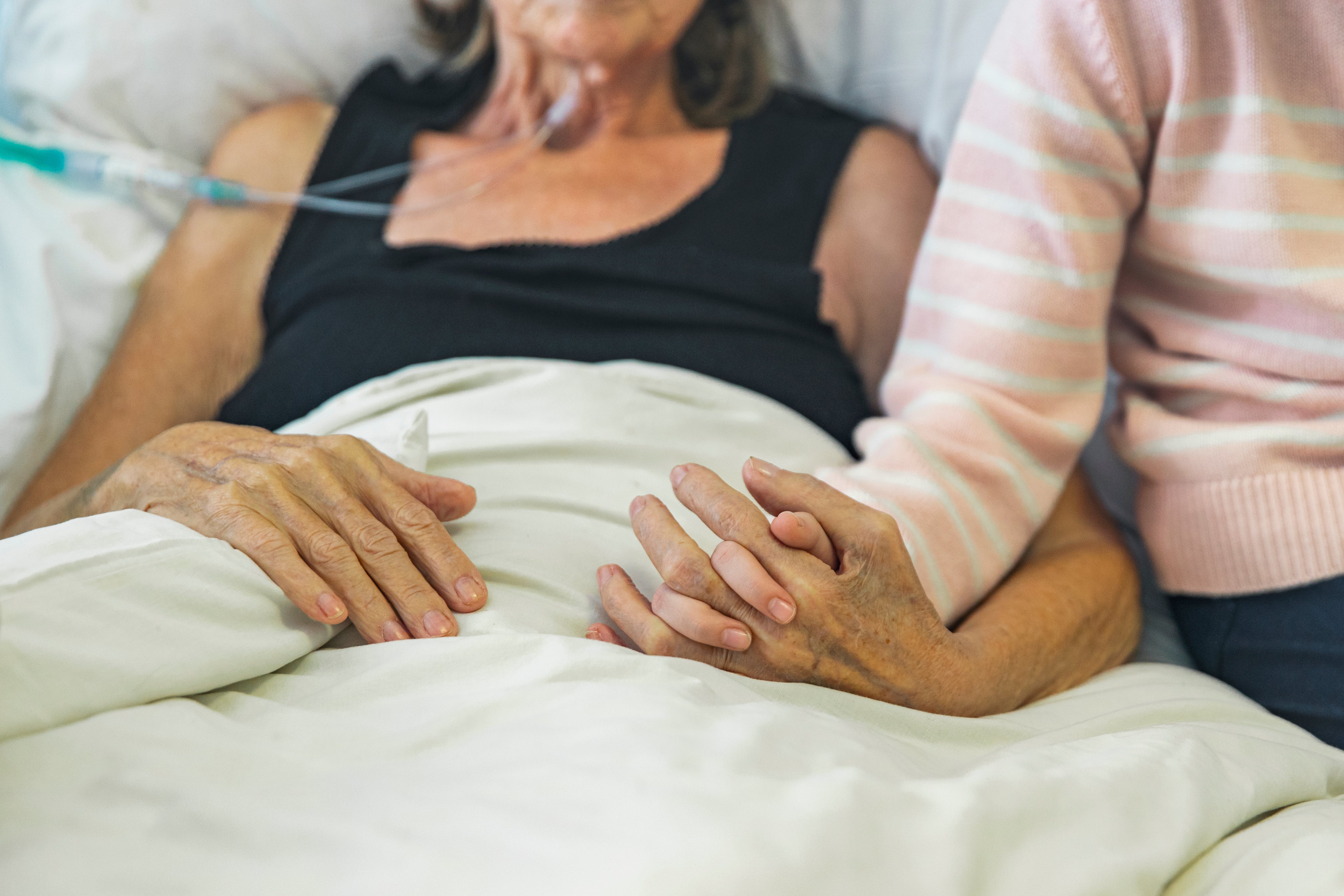 younger woman holding hand of older woman who is in bed with oxygen tubes