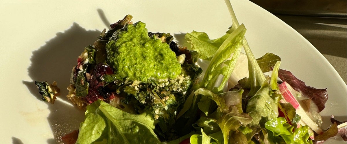 Beet and spinach frittata topped with chive pesto on white plate with green salad.