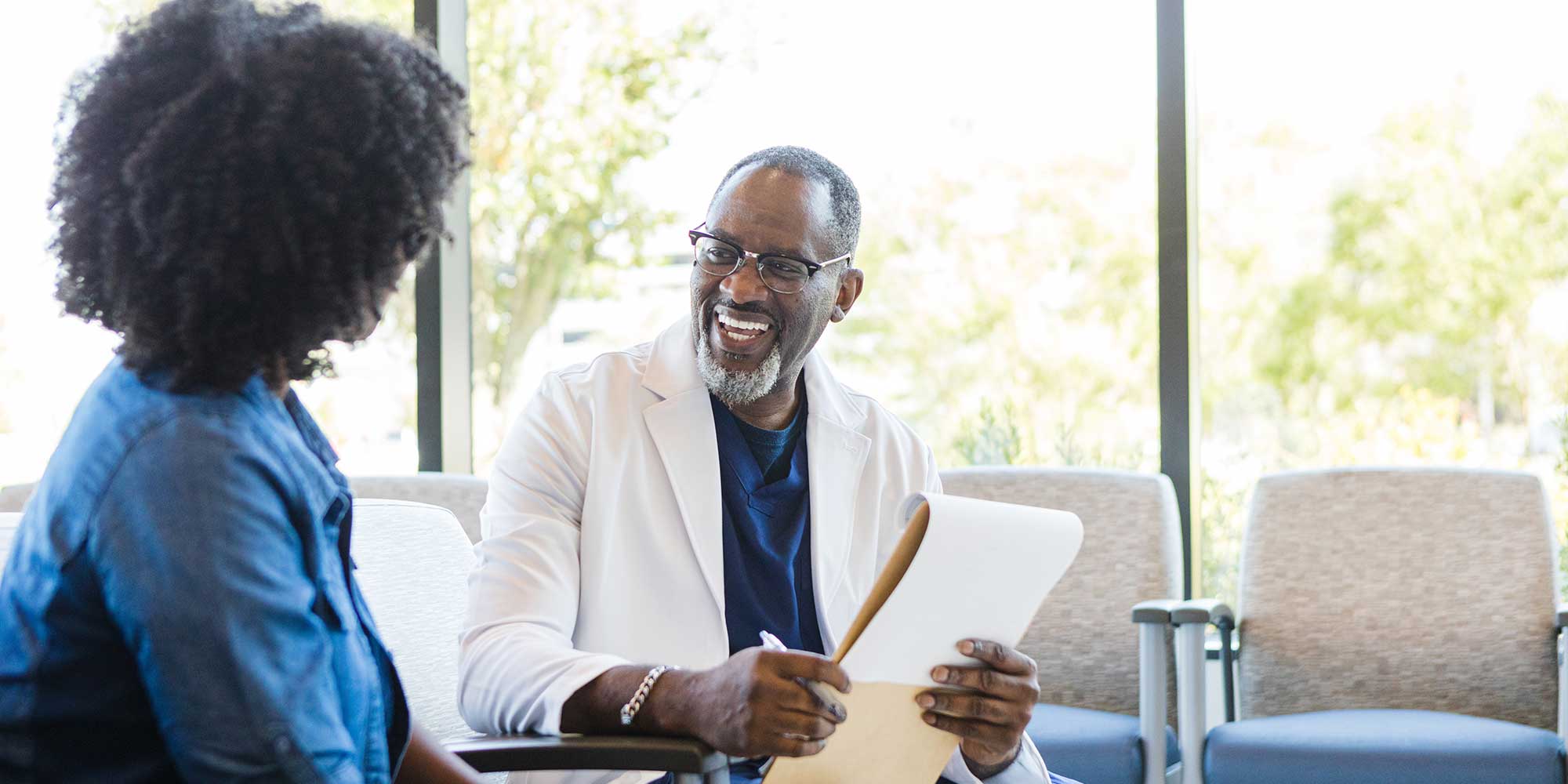 A male physician smiles as he fills out paperwork with a patient