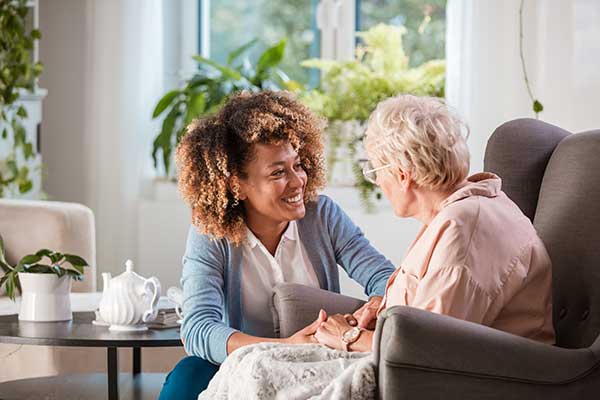 An elderly woman is being taken care of by a younger female nurse in her home
