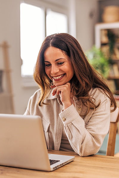 A woman smiles while working on her laptop