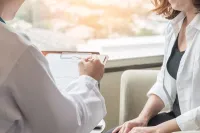 A zoomed in shot of a doctor holding a clipboard while she meets with a patient